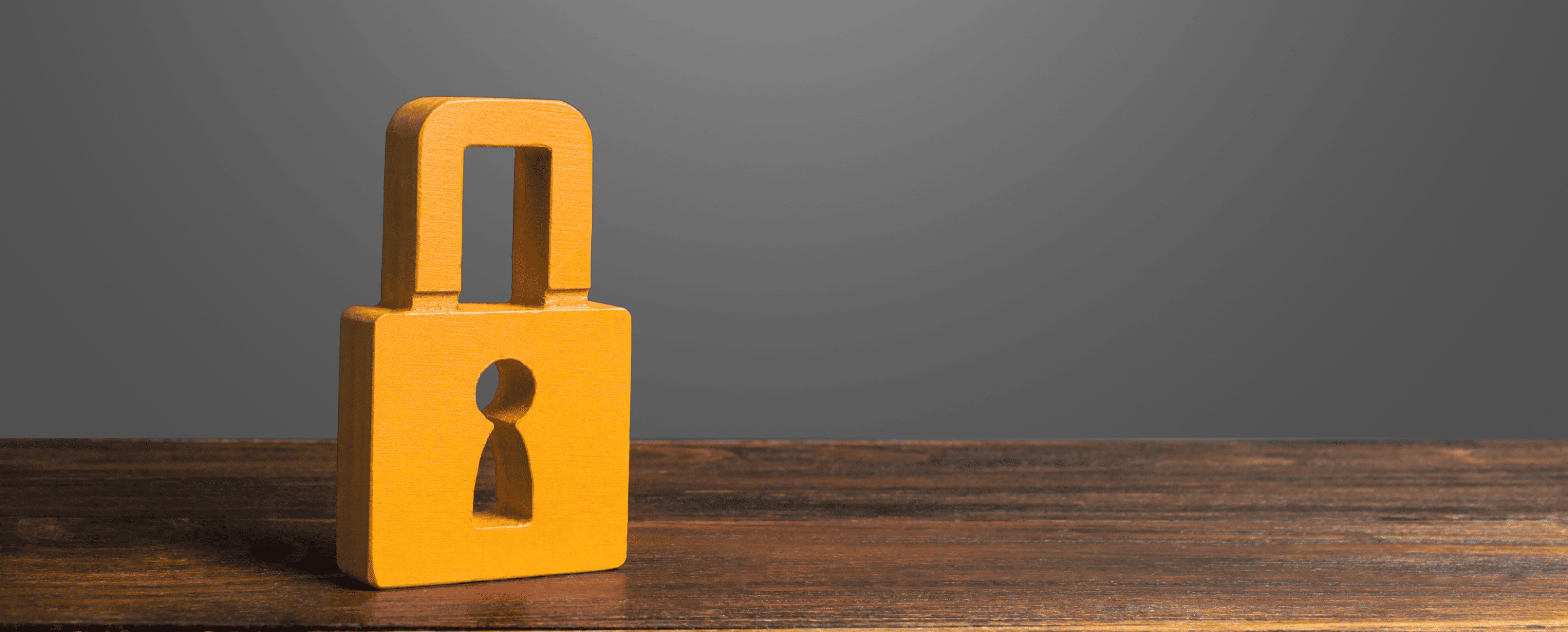 A wooden padlock figurine sits on a wooden surface against a plain gray background.